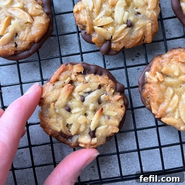 Classic Cinnamon Apple Cake with Warm Spice Glaze 14 Hand reaching for a Florentine cookie with sliced almonds and chocolate resting on a black cooling rack alongside other Florentines.