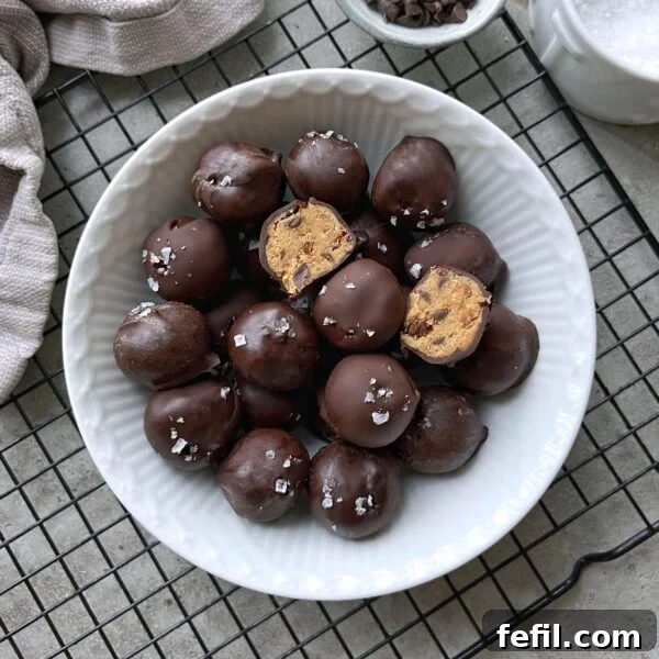 Classic Cinnamon Apple Cake with Warm Spice Glaze 15 A white bowl filled with chocolate-covered cookie dough balls, some topped with flaky sea salt. One ball is cut open.