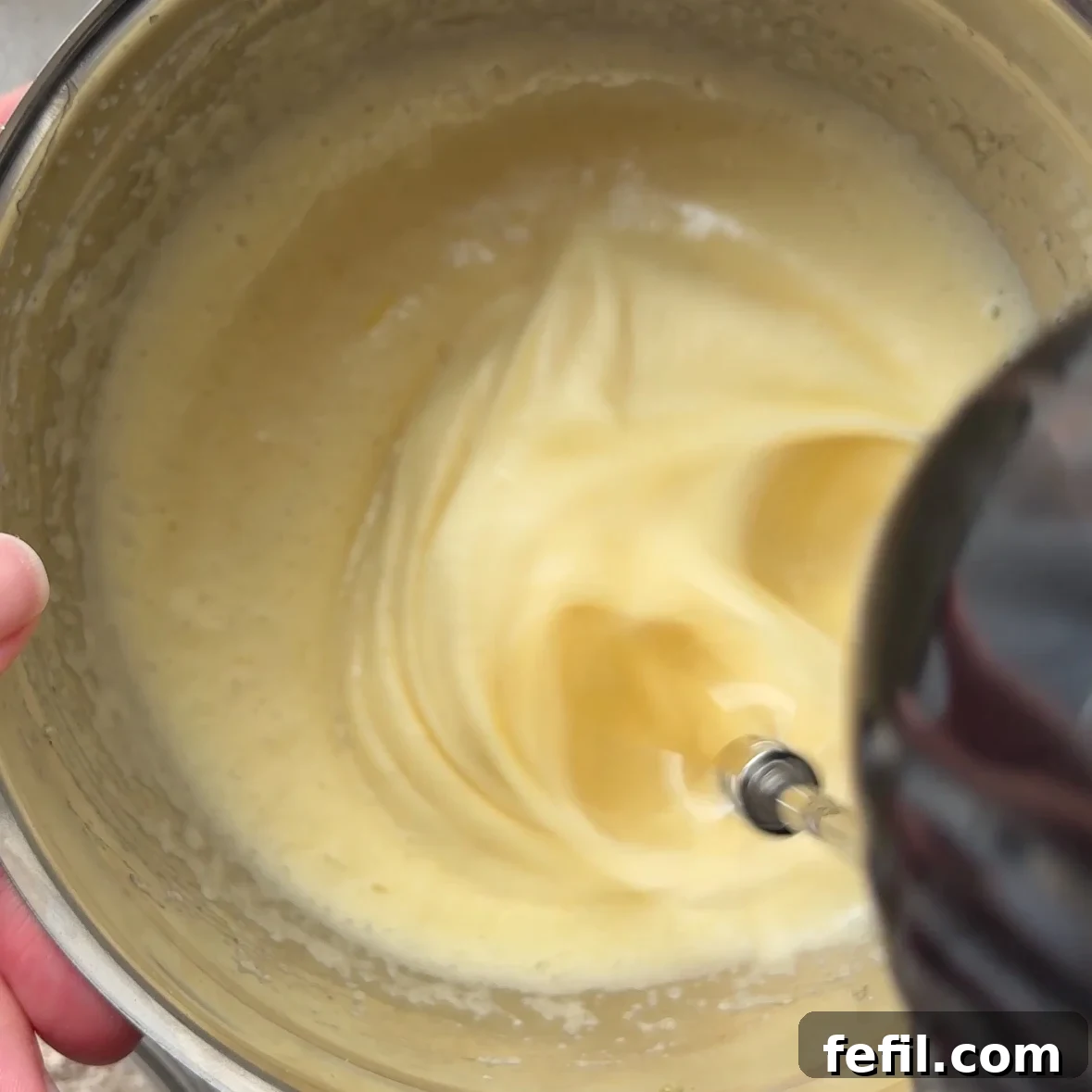 Classic Cinnamon Apple Cake with Warm Spice Glaze 7 A hand holds a metal bowl while an electric mixer blends a creamy Cinnamon Apple Cake batter inside.