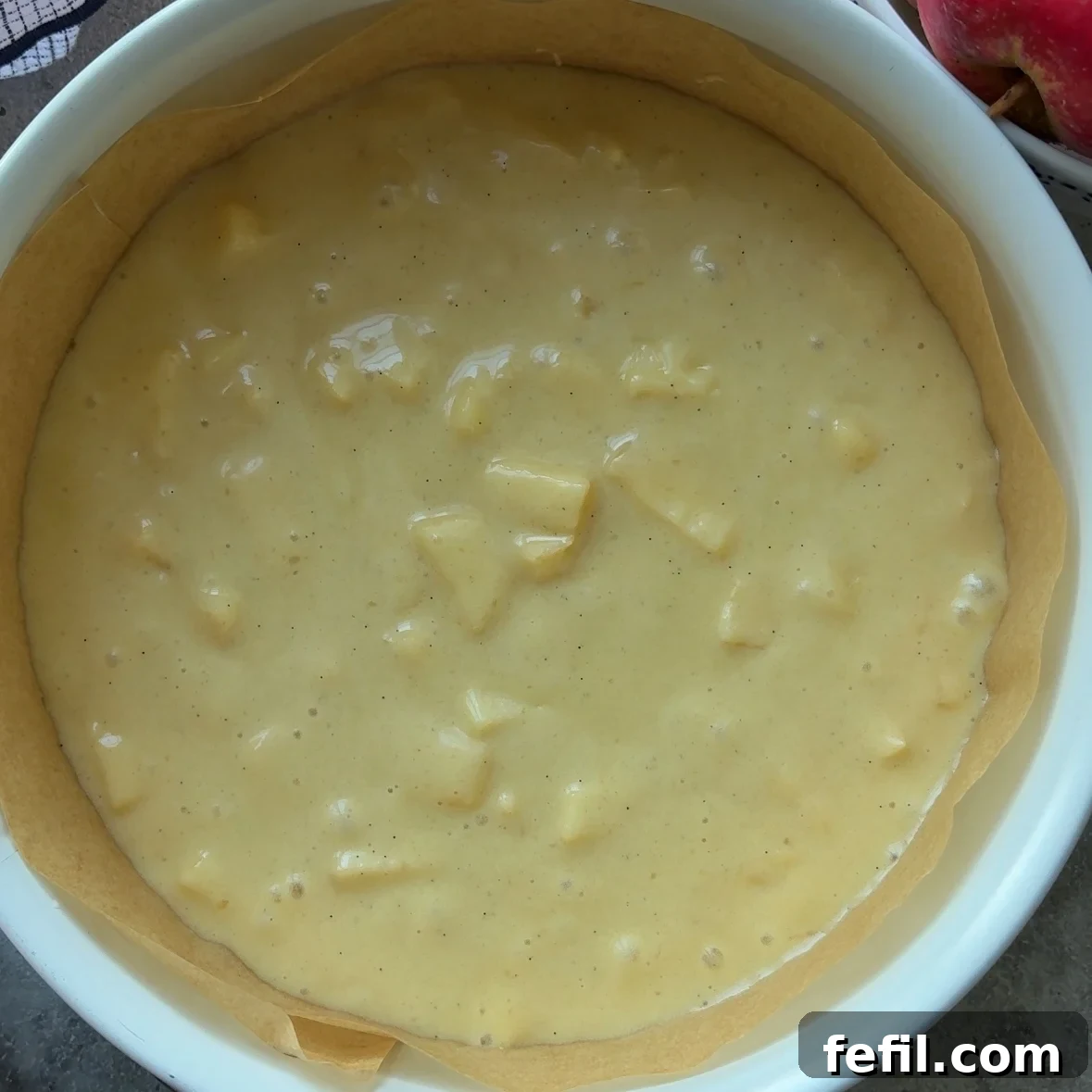 Classic Cinnamon Apple Cake with Warm Spice Glaze 10 Unbaked Cinnamon Apple Cake batter with visible apple chunks in a round baking pan lined with parchment paper.