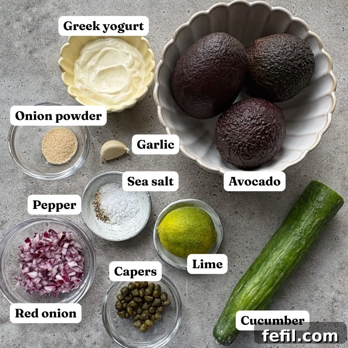 Spooky Halloween Guacamole Recipe for Party Appetizers 5 Ingredients for Halloween Guacamole are laid out including Greek yogurt, avocado, garlic, onion powder, pepper, sea salt, lime, capers, red onion, and cucumber.
