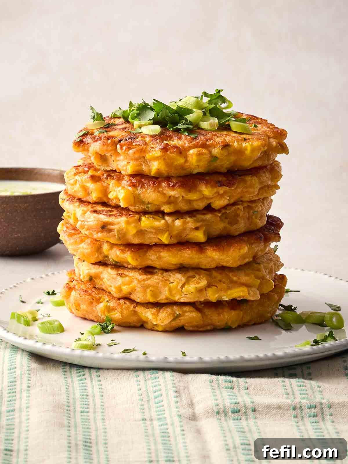 Crispy Sweetcorn Fritters Recipe 3 A tower of Sweetcorn Fritters on a plate, with spring onion on top and garnished with coriander.