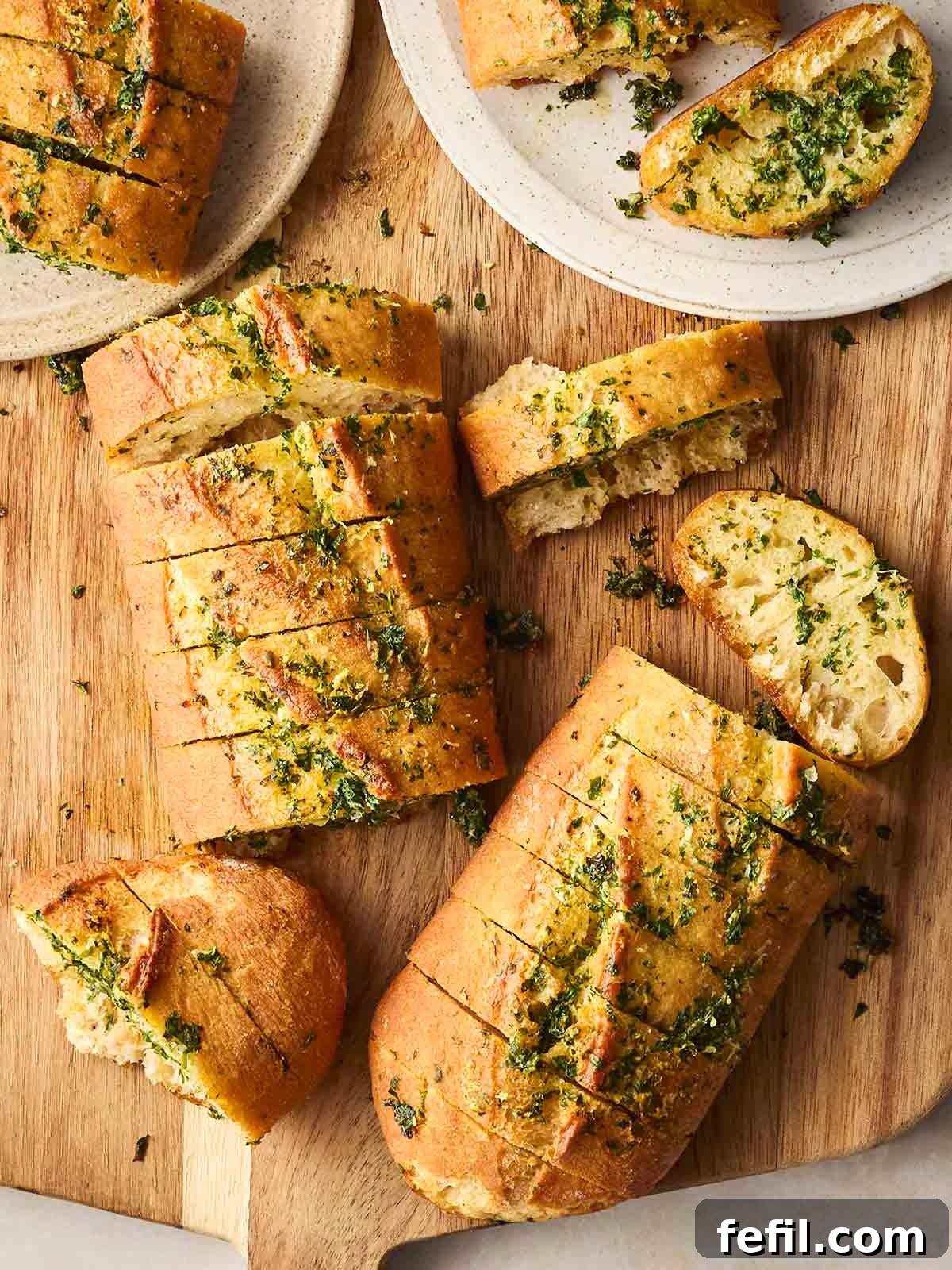 Perfect Crispy Garlic Bread with Herbed Butter 3 A bread board filled with sliced homemade garlic bread, with two plates with a couple of pieces on.