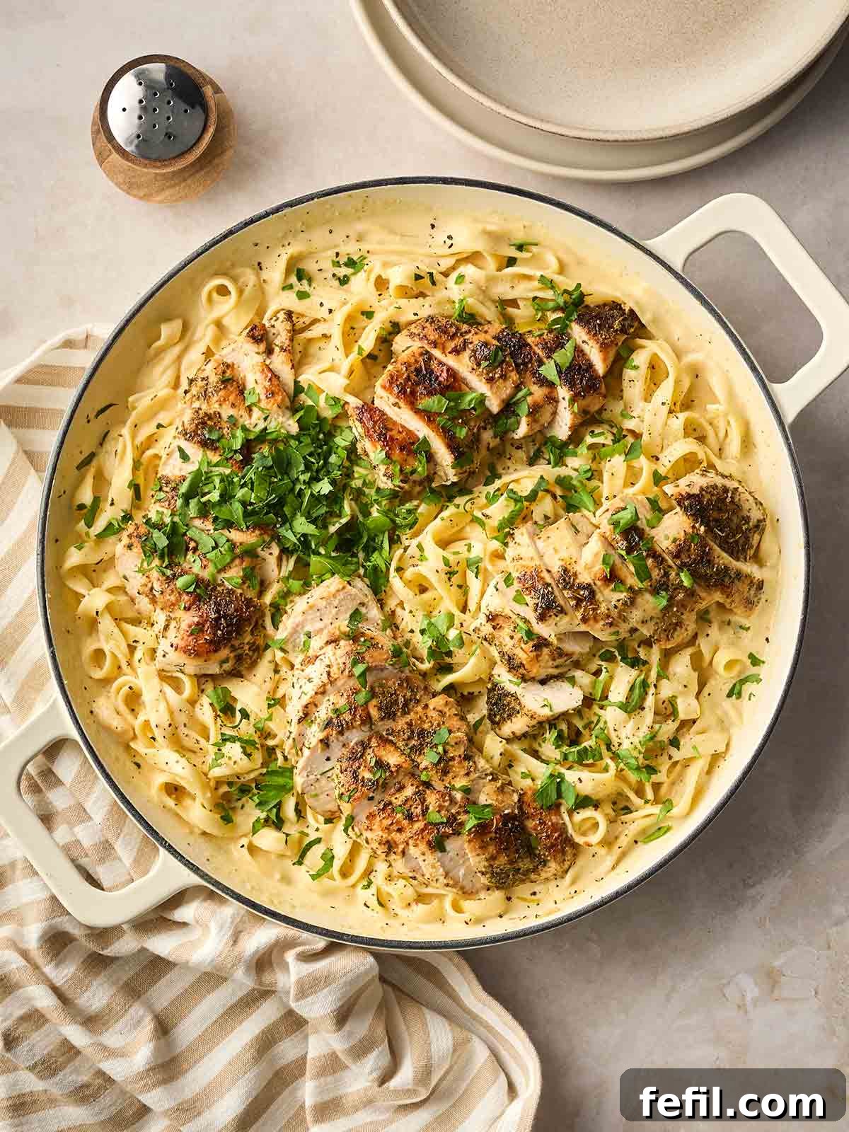 Classic Creamy Chicken Alfredo Recipe 2 A large pan of chicken alfredo with creamy sauce, tagliatelle and chicken breast sliced on top. Ready to serve into bowls, on a dining table.