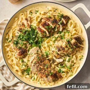 Classic Creamy Chicken Alfredo Recipe 5 A close up of a large white pan filled with Chicken Alfredo, a dish with long tagliatelle pasta, creamy sauce and sliced herby chicken breast on top, with parsley garnished.