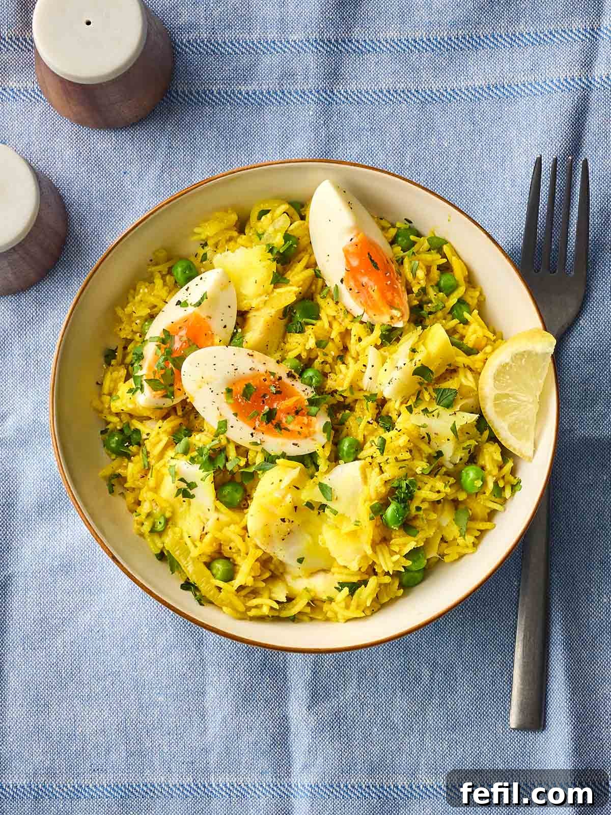 Classic Kedgeree: Smoked Fish, Rice & Curried Eggs 3 A place setting with a blue cloth, with a bowl of Kedgeree and a fork to the side and salt and pepper above.