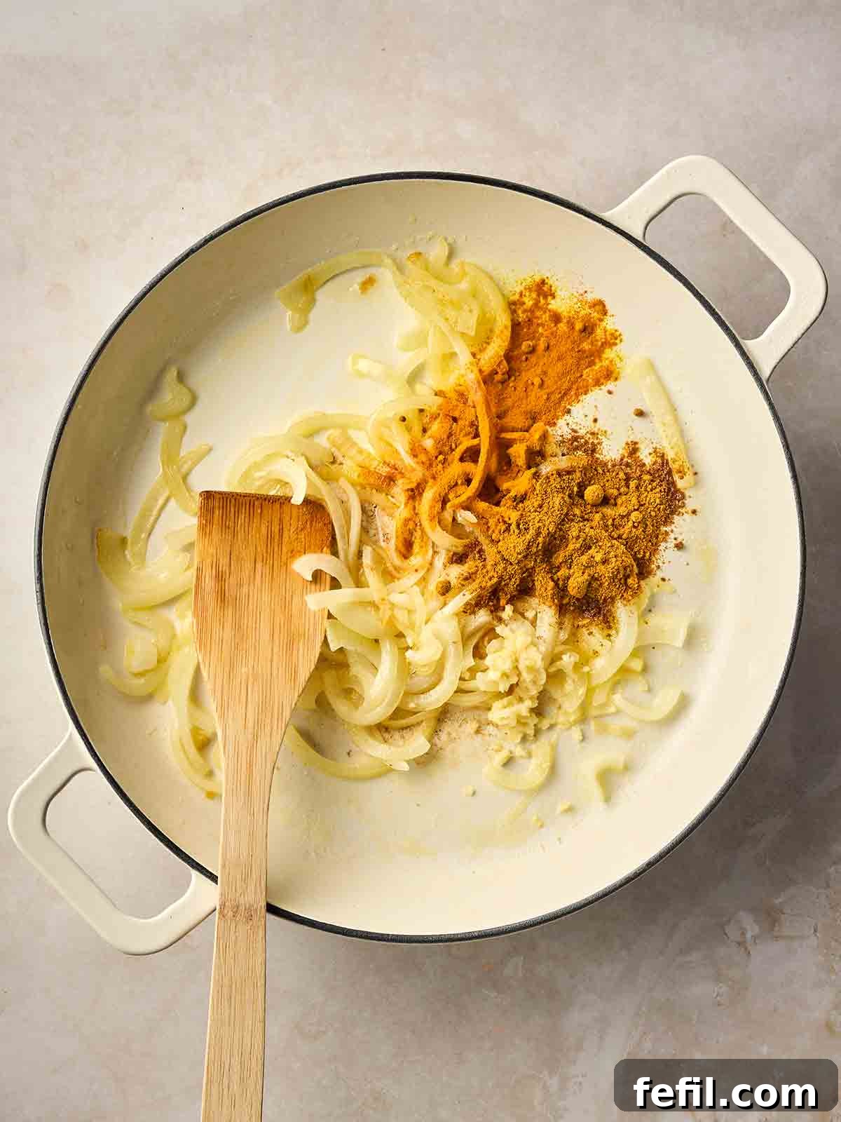 Classic Kedgeree: Smoked Fish, Rice & Curried Eggs 7 A white pan filled with sliced onions and spices, ready to be mixed together with a wooden spatula.