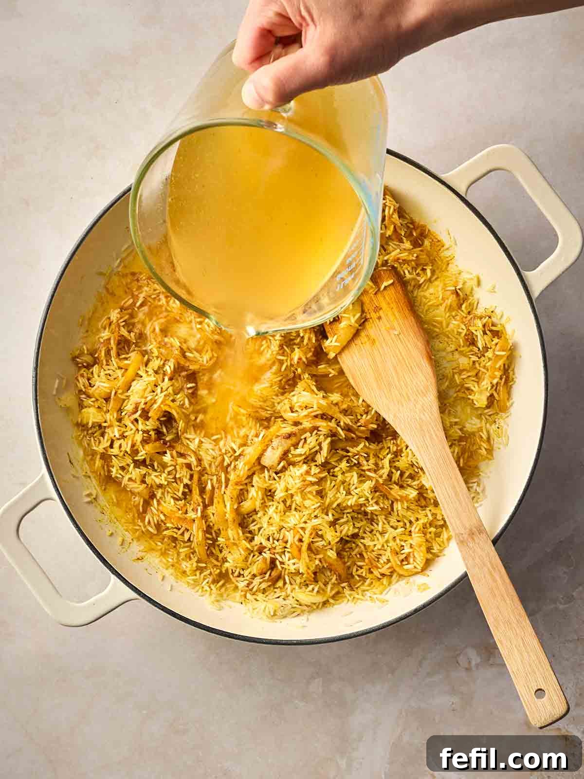 Classic Kedgeree: Smoked Fish, Rice & Curried Eggs 9 A hand pouring stock into a dish with rice, spices and onion.