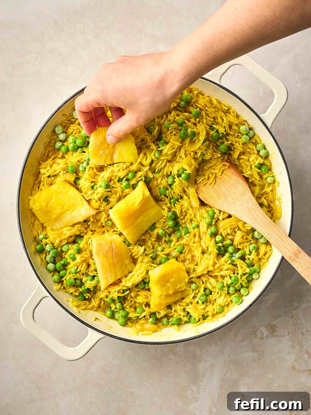 Classic Kedgeree: Smoked Fish, Rice & Curried Eggs 10 A hand placing pieces of smoked haddock with peas into a pan with curried rice for a Kedgeree dish.