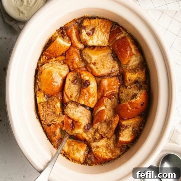 Creamy Slow Cooker Rice Pudding Recipe 8 A big slow cooker pot filled with cooked bread and butter pudding with hot cross buns and a spoon sticking out of it.