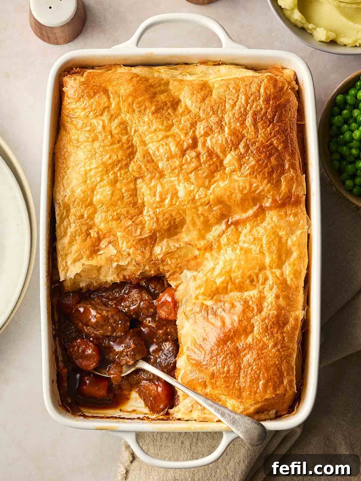 A Steak and Ale Pie with a corner missing to show the filling, on a table, ready to serve up.